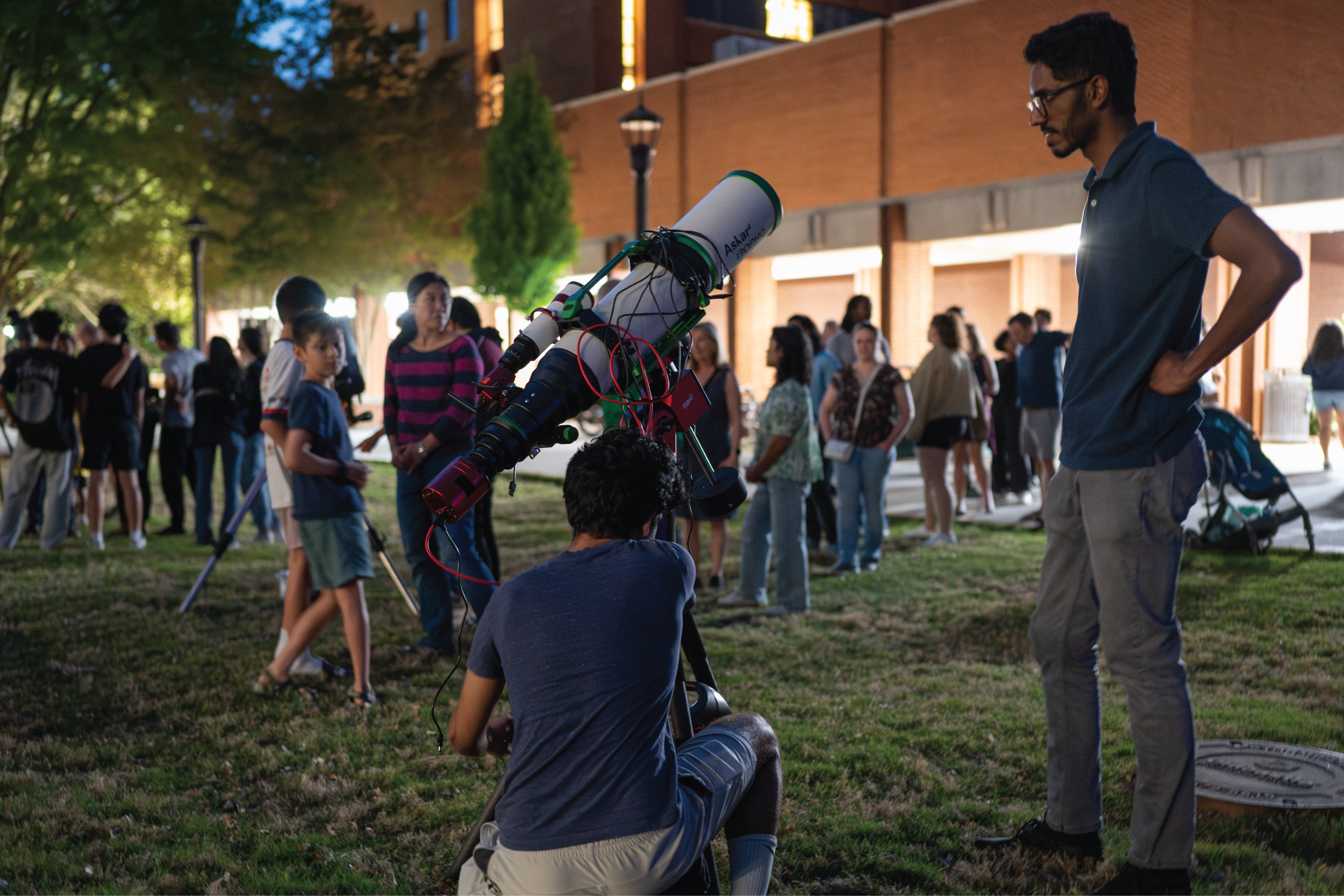 Visitors gather on the Georgia Tech campus lawn at night, lining up to view the sky through a telescope during a public observatory event.
